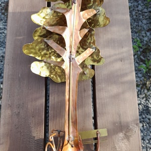 May include: A metal sculpture of a tree with a bicycle underneath. The tree is made of hammered copper and brass and has a rustic, antique look. The bicycle is made of copper and has a simple design.