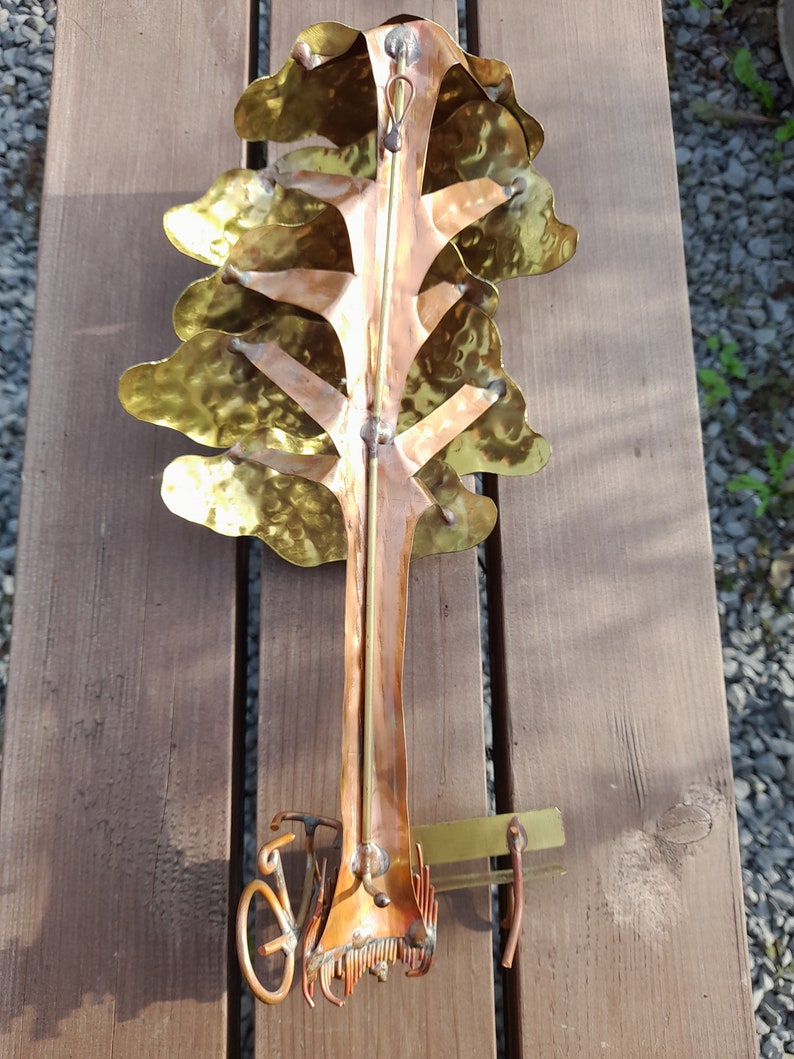May include: A metal sculpture of a tree with a bicycle underneath. The tree is made of hammered copper and brass and has a rustic, antique look. The bicycle is made of copper and has a simple design.