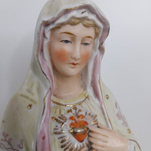 Puede incluir: Una figurita de porcelana de la Virgen Mar&iacute;a, vestida con una t&uacute;nica blanca y rosa con detalles dorados. Tiene un coraz&oacute;n con una corona de espinas en el pecho.