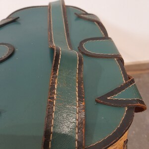 May include: A green leather-covered wicker basket with a brown leather strap and black stitching.
