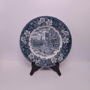 Puede incluir: Un plato de cerámica azul y blanco con un borde floral y una escena de un edificio con un campanario y personas caminando frente a él.