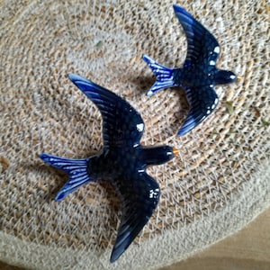 May include: Two blue and white ceramic swallow figurines. The swallows are perched on a woven surface.