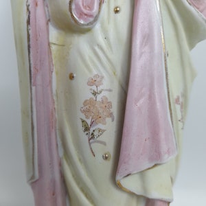 Puede incluir: Una figurita de porcelana de una mujer vestida con un vestido blanco con detalles rosas y florales. El vestido tiene un dise&ntilde;o fluido y la mujer sostiene un objeto peque&ntilde;o en su mano.
