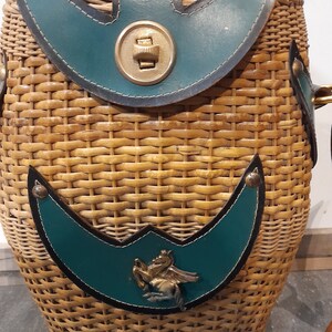 May include: A woven wicker basket with a teal leather flap and a metal button closure. The basket has a teal leather patch with a metal horse design.