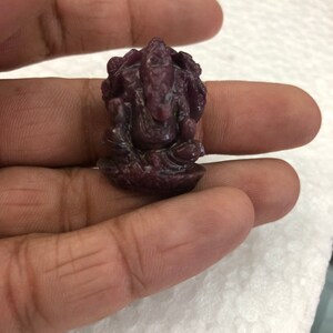 May include: A small, intricately carved figurine of the Hindu deity Ganesha, made from a deep purple gemstone. The figurine is about 2 inches tall and is sitting on a lotus flower.