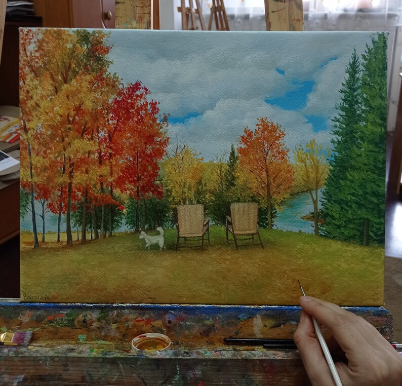Puede incluir: Una pintura de un paisaje oto&ntilde;al con dos sillas y un perro blanco. Los &aacute;rboles est&aacute;n en tonos de rojo, naranja y amarillo. El cielo es azul con nubes blancas. Las sillas son de madera y tienen cojines blancos. El perro corre hacia el lado derecho de la pintura.