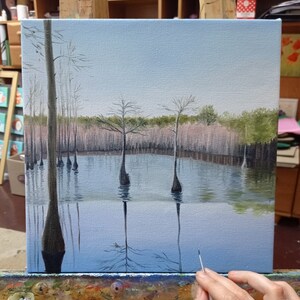 Puede incluir: Una pintura sobre lienzo que representa una escena de pantano con &aacute;rboles altos y delgados reflejados en el agua. El cielo es de un azul claro y el agua es de un azul verdoso claro. Los &aacute;rboles son de color marr&oacute;n oscuro y el agua es de un azul verdoso claro.