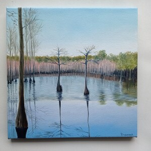 Puede incluir: Una pintura que representa una escena de pantano con tres cipreses en el agua. El agua es de color azul claro y el cielo es de color azul claro. Los &aacute;rboles est&aacute;n desnudos y el agua est&aacute; tranquila. La pintura est&aacute; firmada "Brannock" en la esquina inferior derecha.