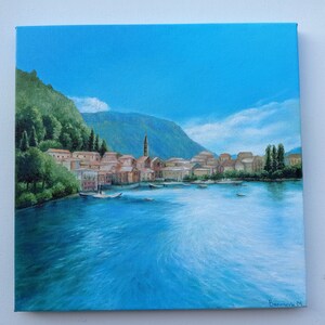 Puede incluir: Una pintura de un peque&ntilde;o pueblo en un lago con una monta&ntilde;a en el fondo. El cielo es azul y el agua es azul claro. Hay &aacute;rboles en la orilla y edificios en el pueblo. La pintura est&aacute; firmada "Bonnerich M."