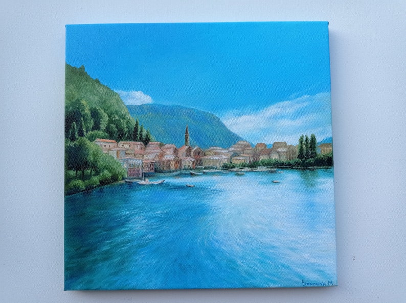 Puede incluir: Una pintura de un peque&ntilde;o pueblo en un lago con una monta&ntilde;a en el fondo. El cielo es azul y el agua es azul claro. Hay &aacute;rboles en la orilla y edificios en el pueblo. La pintura est&aacute; firmada "Bonnerich M."