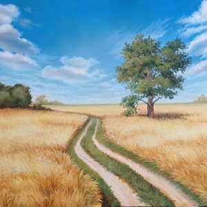 Puede incluir: Un camino de tierra serpentea a trav&eacute;s de un campo de trigo dorado bajo un cielo azul con nubes blancas. Un &aacute;rbol solitario se alza en el campo.