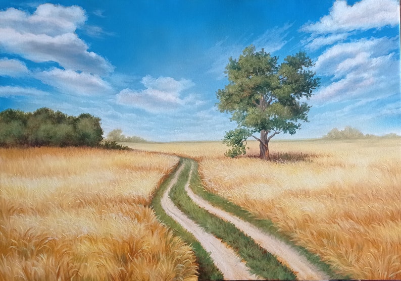 Puede incluir: Un camino de tierra serpentea a trav&eacute;s de un campo de trigo dorado bajo un cielo azul con nubes blancas. Un &aacute;rbol solitario se alza en el campo.