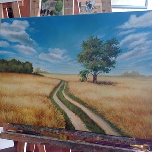 Puede incluir: Una pintura de un camino de tierra que serpentea a trav&eacute;s de un campo de trigo dorado. Un solo &aacute;rbol se alza en medio del campo, con un cielo azul y nubes blancas en el fondo.