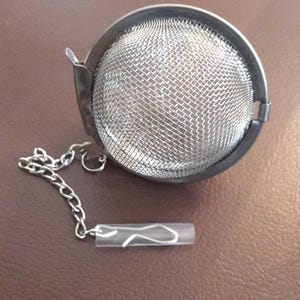 May include: A silver tea infuser with a mesh ball and a chain. The infuser has a hinged lid and a small hook on the chain.