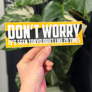 May include: A rectangular sticker with a yellow background and black diagonal accents. The text in bold white capital letters reads DON'T WORRY, followed by the text IV'E SEEN TOKYO DRIFT LIKE 20 TIMES in smaller white capital letters.