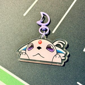 May include: A clear acrylic charm featuring a cartoon character with a pink face, purple eyes, and a red gem. The charm has a purple clasp and a silver ring. The character is peeking over the edge.