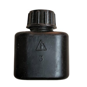 May include: A black, square-shaped bottle with a ridged cap. The bottle has a warning symbol and the number 3 printed on the front. The bottle is made of a matte black material.