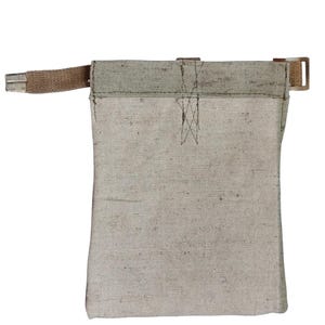 Op de afbeelding: Een beige canvas tas met een bruine riem en metalen gesp. De tas heeft een rechthoekige vorm met een versterkte bovenkant en een gestikt ontwerp. De riem is aan de bovenkant van de tas bevestigd.