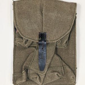 Può includere: Una borsa militare in tela verde con una cinghia e una fibbia in pelle nera. La borsa ha una patta che si ripiega e si chiude con la cinghia.