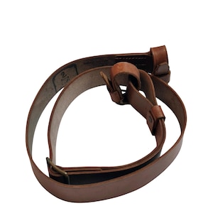 May include: A brown leather strap with a buckle and a loop. The strap is curved and appears to be made of a durable material. The strap is likely for a bag or other accessory.