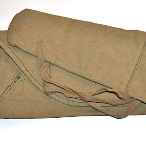 Puede incluir: Una bolsa de lona beige con cierre de cordón y una correa larga. La bolsa está doblada y atada con la correa.