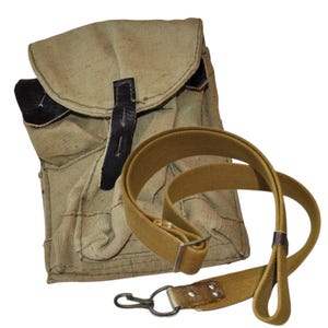 Könnte beinhalten: Eine khakifarbene Canvas-Tasche mit Klappe und schwarzem Lederriemen. Ein passender khakifarbener Riemen mit Metallverschluss ist ebenfalls enthalten. Die Tasche hat eine Vintage- oder Militär-Ästhetik.