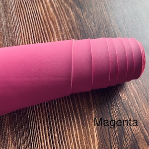 Puede incluir: Un rollo de tela de imitaci&oacute;n de cuero de color magenta. La tela tiene una superficie texturizada.