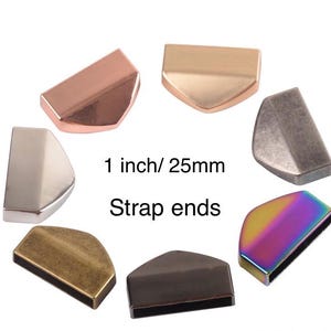 Pode incluir: Uma coleção de extremidades de correias metálicas em várias cores, incluindo cobre, ouro, prata e iridescente. As extremidades da correia têm aproximadamente 25 mm de comprimento, com o texto "1 inch / 25mm" e "Strap ends" em preto.