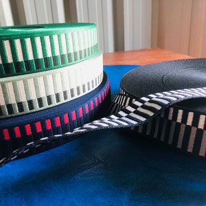 Puede incluir: Cuatro rollos de cinta elástica estampada en verde, blanco, negro y rojo, y un rollo de cinta elástica negra con un patrón de cuadros blancos y negros.