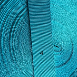 May include: Close-up of turquoise blue webbing, showing the rolled up webbing and a straight section with the number "4" printed on it.