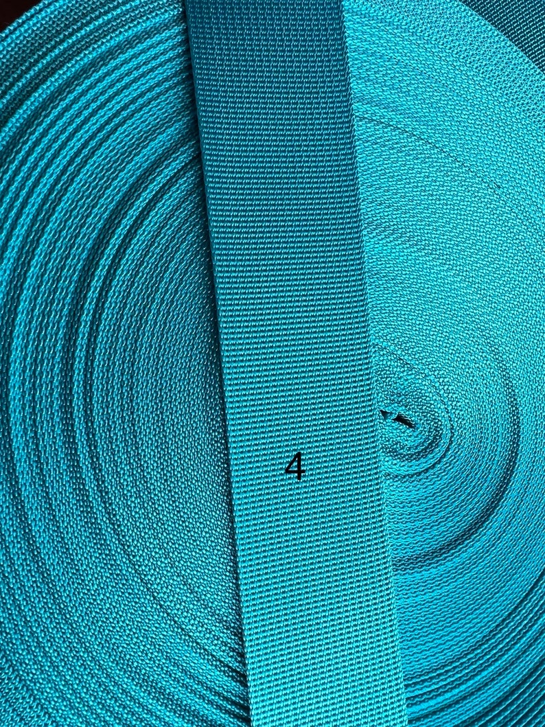 May include: Close-up of turquoise blue webbing, showing the rolled up webbing and a straight section with the number "4" printed on it.