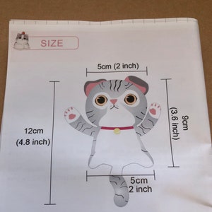 May include: A gray and white cat with a red collar and a yellow bell. The cat is 9 cm (3.6 inches) tall and 12 cm (4.8 inches) wide. The cat's tail is 5 cm (2 inches) long.