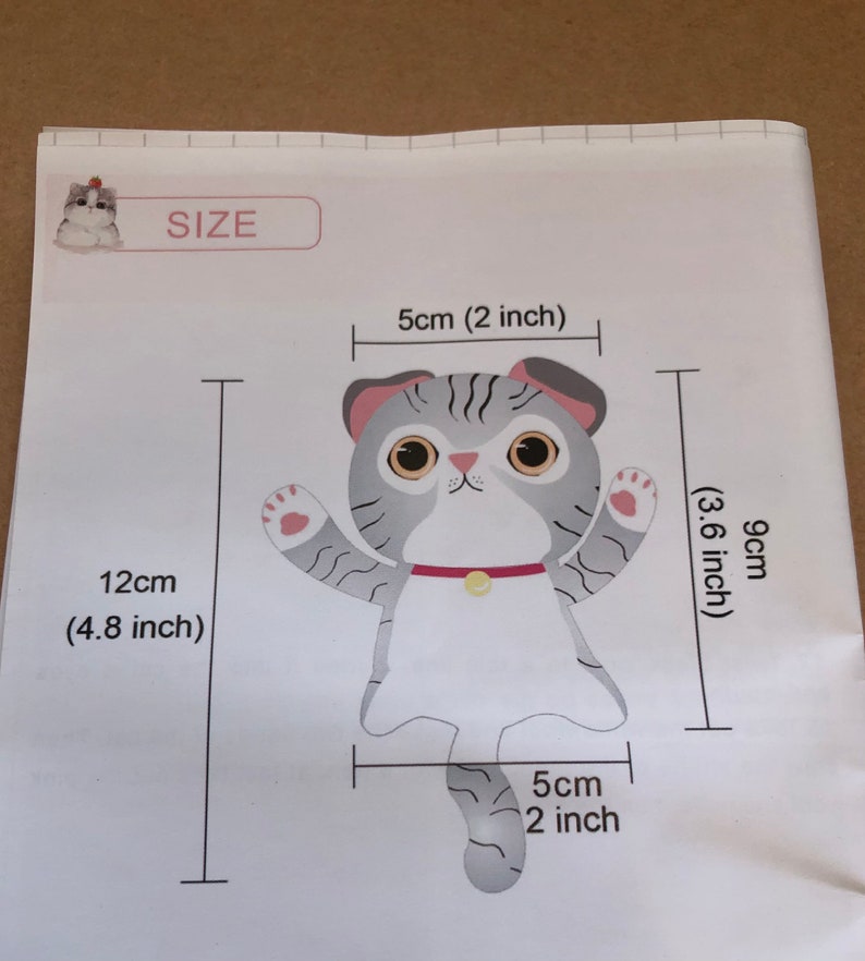 May include: A gray and white cat with a red collar and a yellow bell. The cat is 9 cm (3.6 inches) tall and 12 cm (4.8 inches) wide. The cat's tail is 5 cm (2 inches) long.