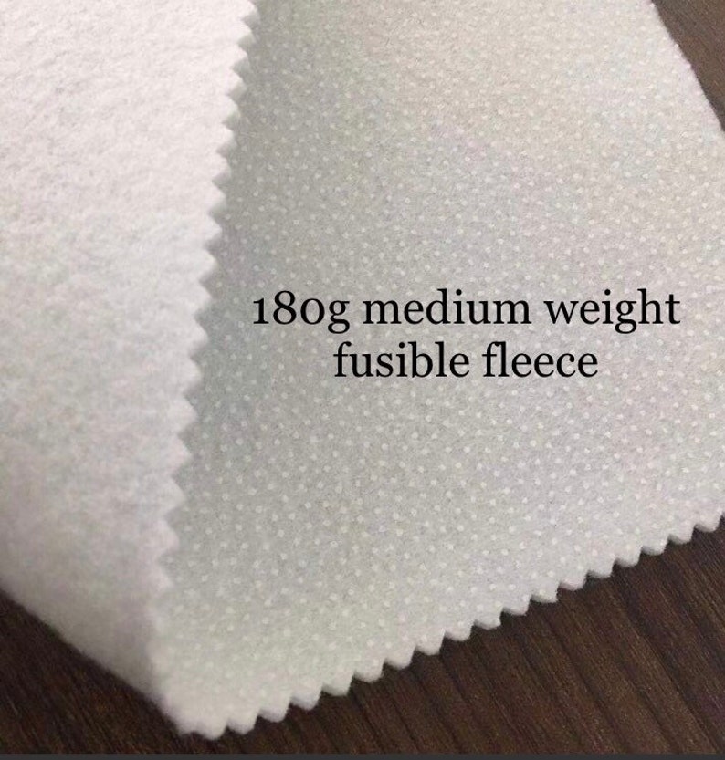 K&ouml;nnte beinhalten: Wei&szlig;er, schmelzbarer Fleece-Stoff mit gepunkteter Textur. Der Stoff ist mit "180g mittelschwerer schmelzbarer Fleece" beschriftet.