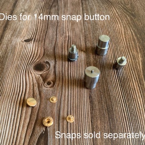 Op de afbeelding: Set metalen matrijzen voor het plaatsen van 14 mm drukknopen. De matrijzen zijn zilverkleurig en hebben een gladde afwerking. De afbeelding toont ook vier goudkleurige drukknopen. De tekst "Dies for 14mm snap button" en "Snaps sold separately" is zichtbaar in de afbeelding.