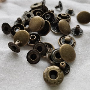 Puede incluir: Primer plano de un mont&oacute;n de botones a presi&oacute;n de metal dorado antiguo. Los botones a presi&oacute;n son redondos y tienen un dise&ntilde;o decorativo alrededor del borde.