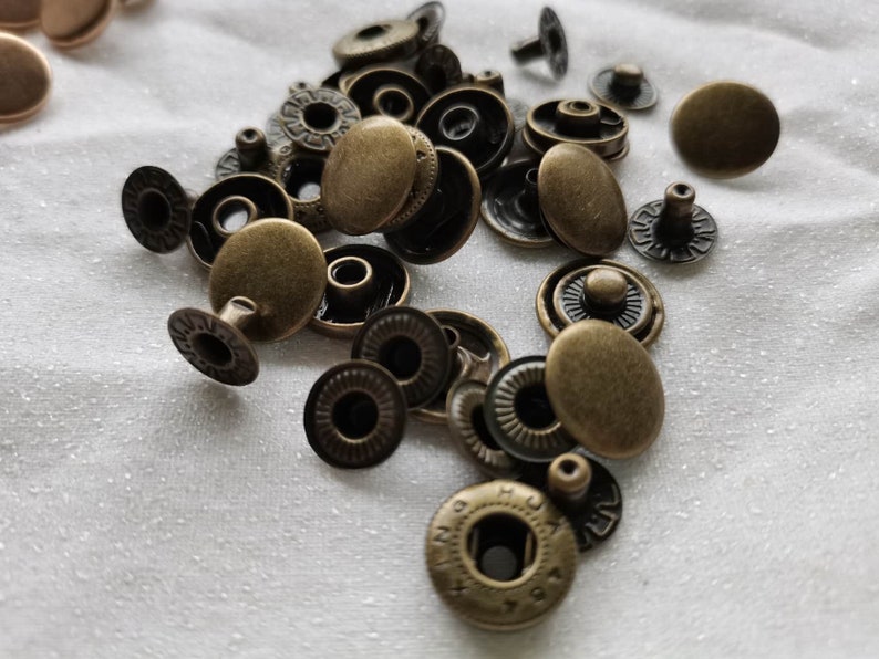 Puede incluir: Primer plano de un mont&oacute;n de botones a presi&oacute;n de metal dorado antiguo. Los botones a presi&oacute;n son redondos y tienen un dise&ntilde;o decorativo alrededor del borde.