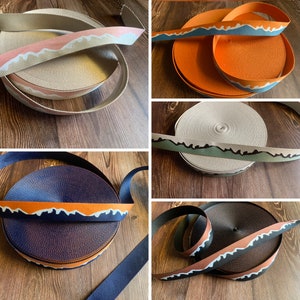Peut inclure: Quatre rouleaux de sangle avec un motif de chaîne de montagnes. La sangle est de différentes couleurs, notamment beige, orange, marron et bleu marine.