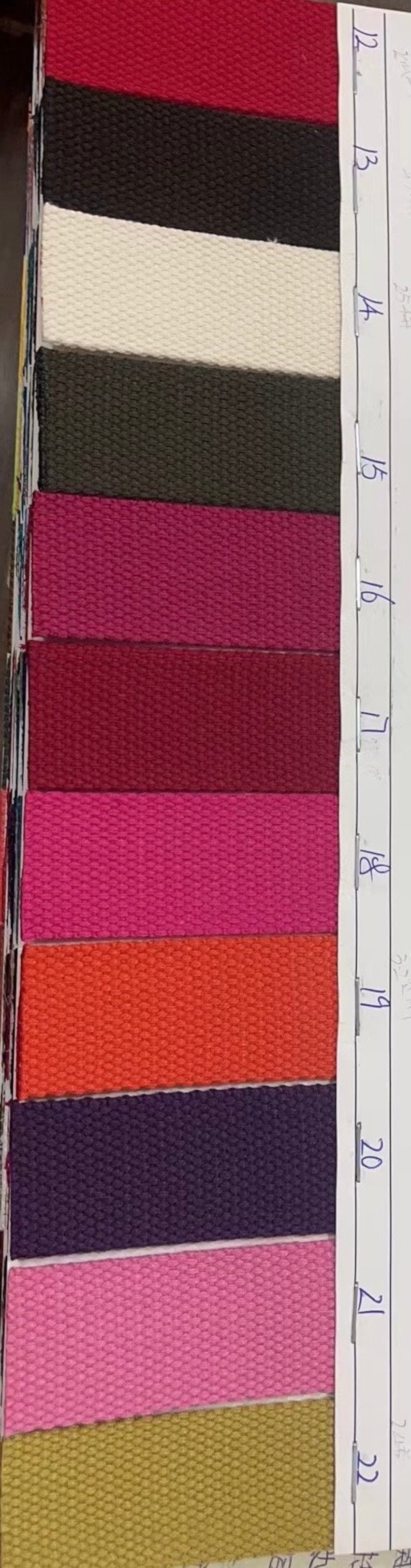 May include: A sample card with numbered swatches of different colored woven webbing. The colors include red, black, white, green, pink, burgundy, orange, purple, and gold.