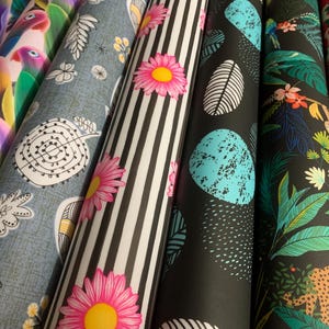Puede incluir: Una colección de seis rollos de tela con diversos patrones que incluyen loros coloridos, hojas grises, rayas blancas y negras con margaritas rosas, formas abstractas turquesas sobre fondo negro, un estampado de selva con un leopardo y fresas rojas.