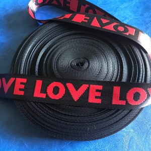 May include: Black and red elastic ribbon with the word "LOVE" repeated in red lettering.
