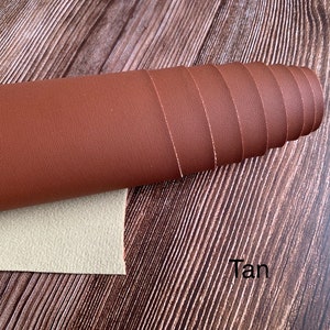 Puede incluir: Un rollo de tela de cuero sint&eacute;tico de color marr&oacute;n claro. La tela tiene una superficie texturizada y est&aacute; enrollada sobre una superficie de madera.