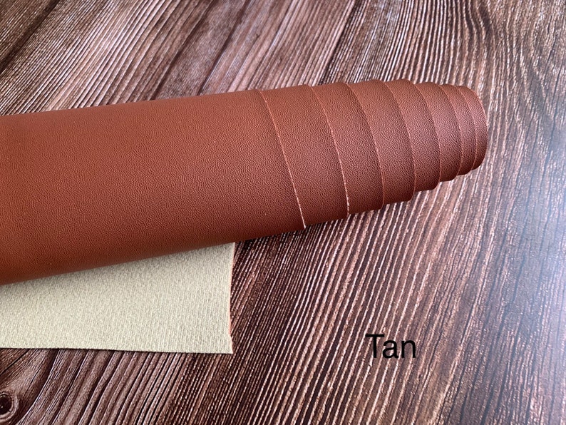 Puede incluir: Un rollo de tela de cuero sint&eacute;tico de color marr&oacute;n claro. La tela tiene una superficie texturizada y est&aacute; enrollada sobre una superficie de madera.