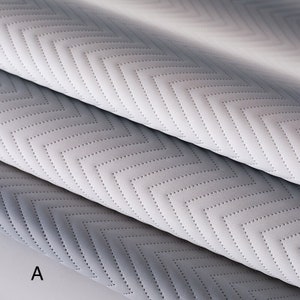 May include: Two pieces of fabric with a chevron pattern. The fabric is a light gray color and has a subtle texture. The fabric is folded in half and the letter "A" is visible in the bottom left corner.