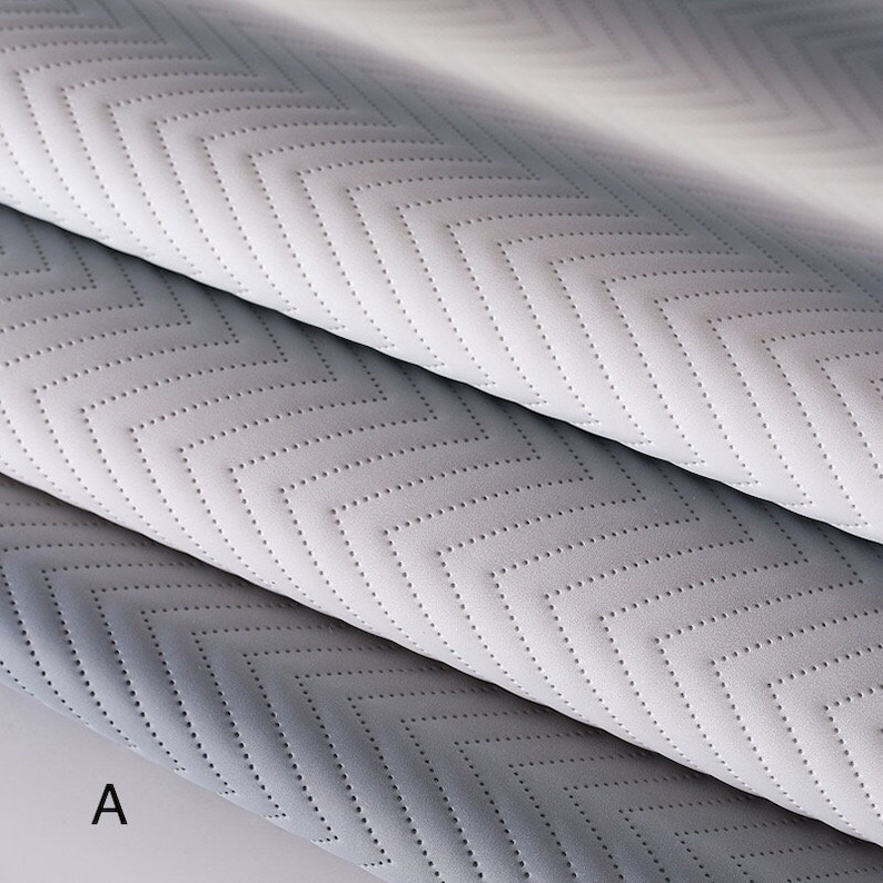 May include: Two pieces of fabric with a chevron pattern. The fabric is a light gray color and has a subtle texture. The fabric is folded in half and the letter "A" is visible in the bottom left corner.