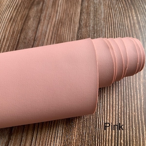 Puede incluir: Un rollo de tela de imitaci&oacute;n de cuero rosa con una superficie texturizada. Rosa.