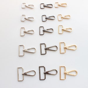 Puede incluir: Un juego de 12 cierres giratorios de metal plateado, dorado y negro. Los cierres están dispuestos en tres filas de cuatro, con cada fila presentando un color diferente.