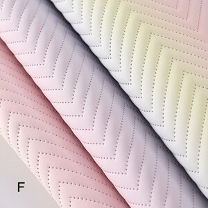 May include: Three rolls of fabric with a chevron pattern in shades of pink, purple, and yellow. The fabric has a subtle texture and a gradient effect.