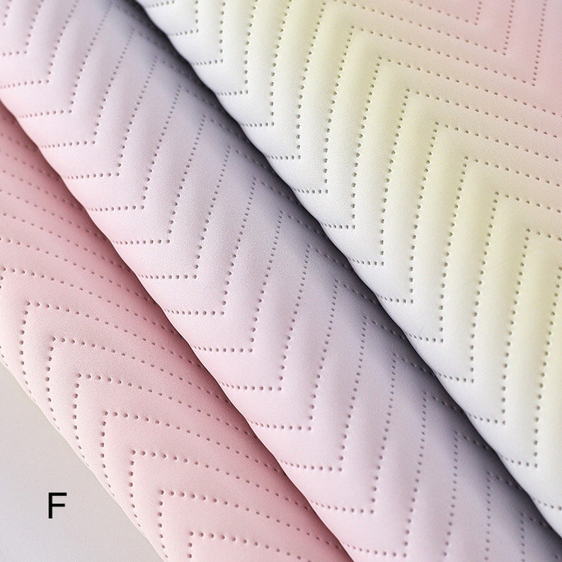 May include: Three rolls of fabric with a chevron pattern in shades of pink, purple, and yellow. The fabric has a subtle texture and a gradient effect.