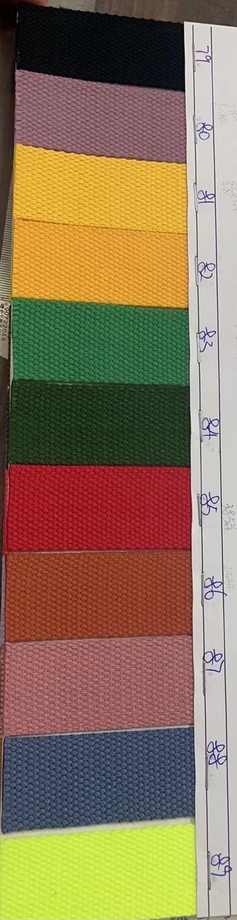 May include: A color chart of 11 different fabric swatches. The swatches are arranged vertically from top to bottom. The colors are black, purple, yellow, orange, green, dark green, red, brown, pink, blue, and neon green. The chart is labeled with numbers 71, 80, 81, 82, 83, 84, 85, 86, 87, 88, and 89.